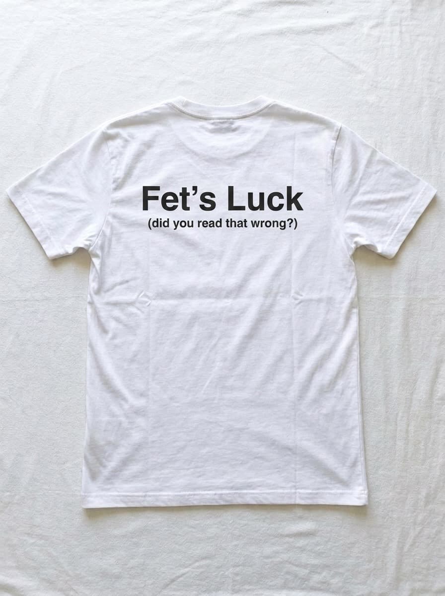 Back of a white t-shirt printed with the words Fet's Luck in large black type, with the line did you read that wrong underneath.