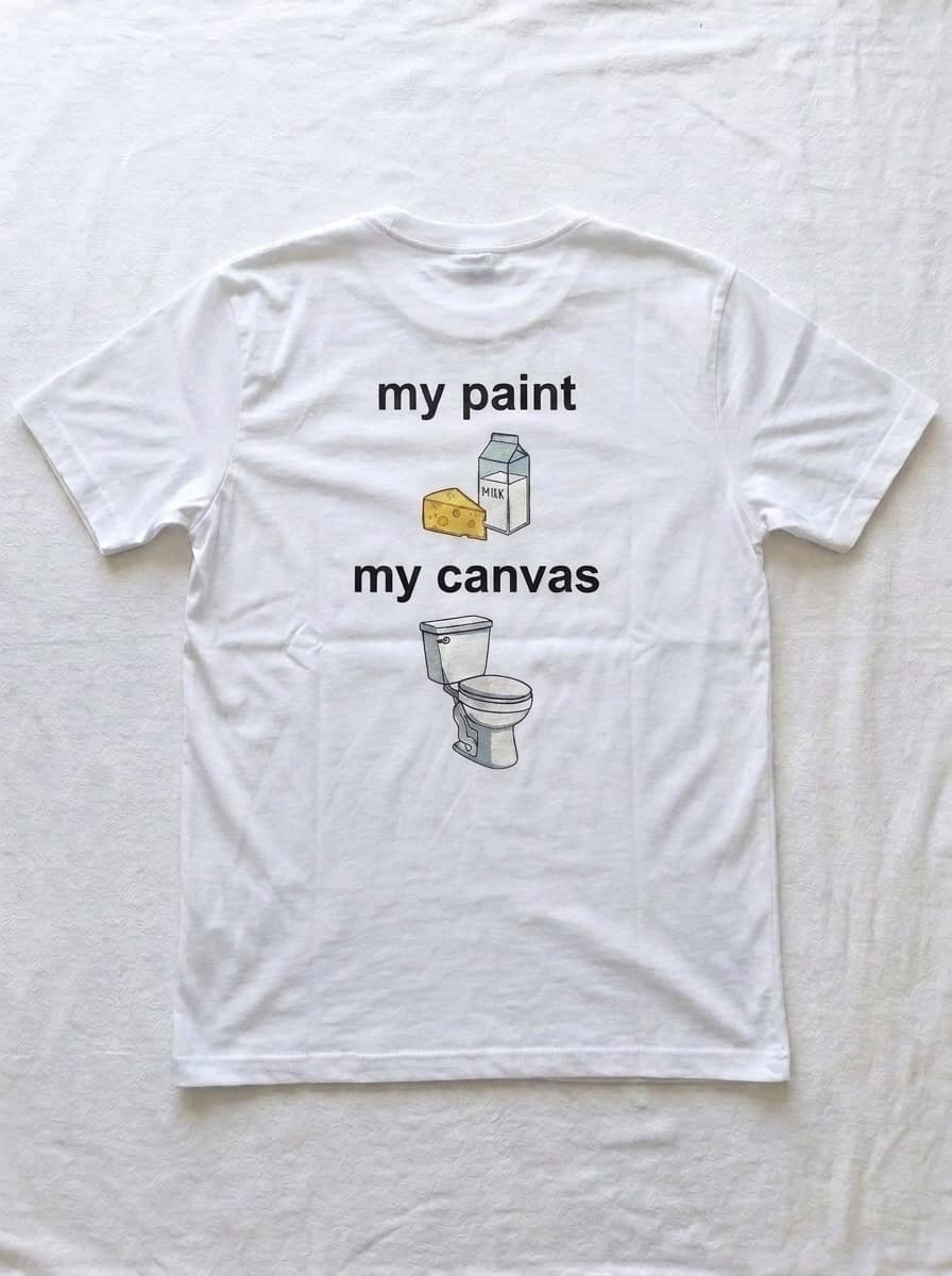 Back of a white t-shirt printed with the words my paint above a carton of milk and a wedge of cheese, and the words my canvas above a toilet.