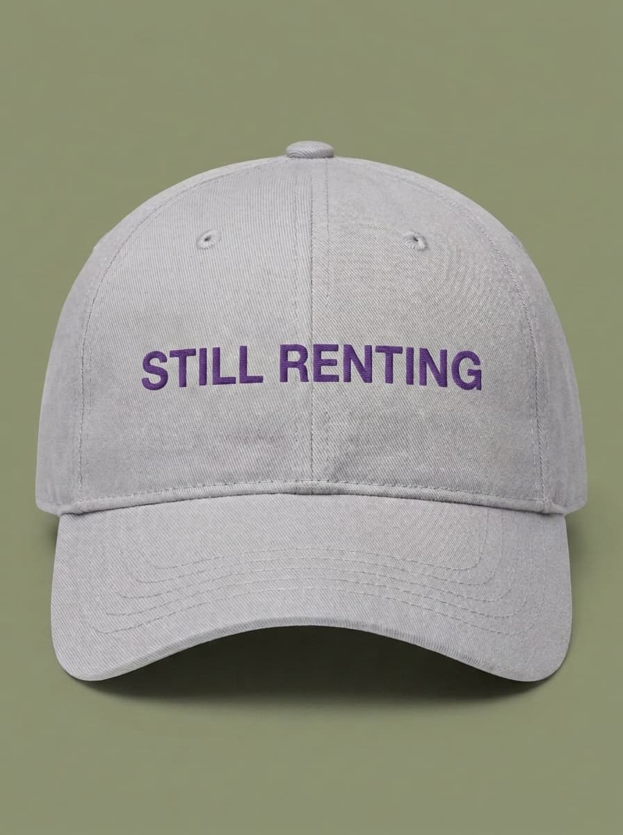 Light grey dad hat embroidered in purple with STILL RENTING.